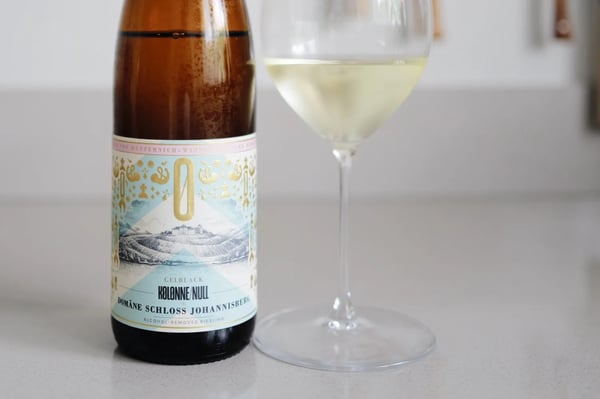 Bottle of Kolonne Null Gelblack alcohol-free Riesling next to a glass of white wine on a light kitchen counter