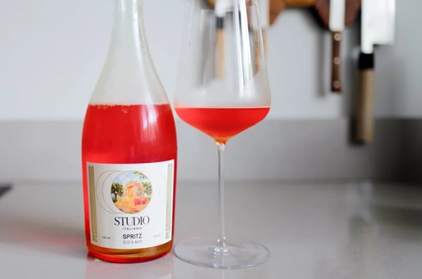 Bottle of Kolonne Null Spritz Studio Italiano beside a glass of rosé-orange spritz on a countertop