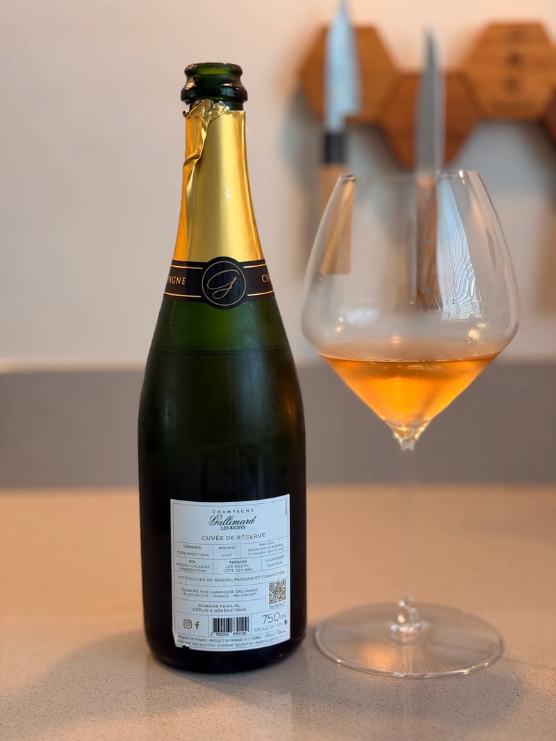 Back label of Gallimard Cuvée de Réserve Blanc de Noirs beside a glass of copper-coloured champagne