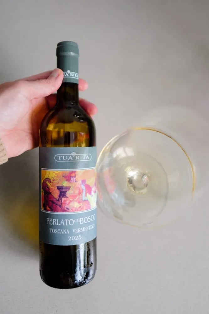 A glass of Perlato del Bosco Vermentino 2025 tilted beside the bottle