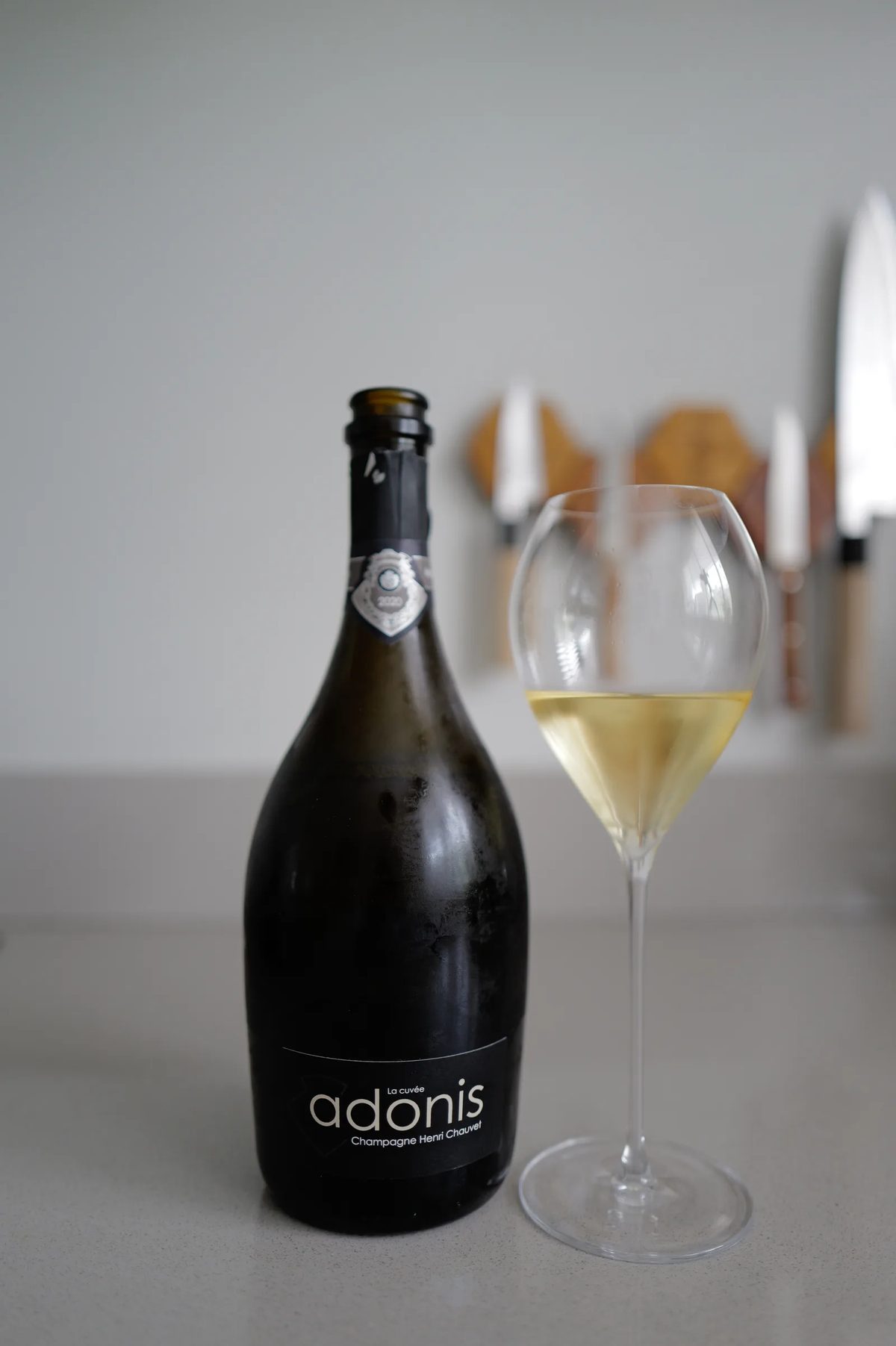 Fles Henri Chauvet Adonis 2020 naast een glas champagne