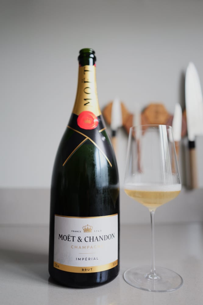 Moët & Chandon Brut Impérial naast een wijnglas met goudgele champagne en fijne mousse